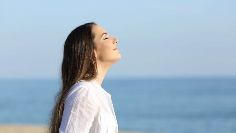 Frau atmet mit Meer im Hintergrund (Richtiges Atmen)