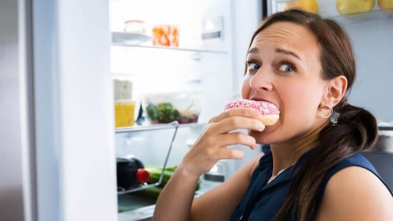 Frau ist verstohlen einen Donut aus dem Kühlschrank