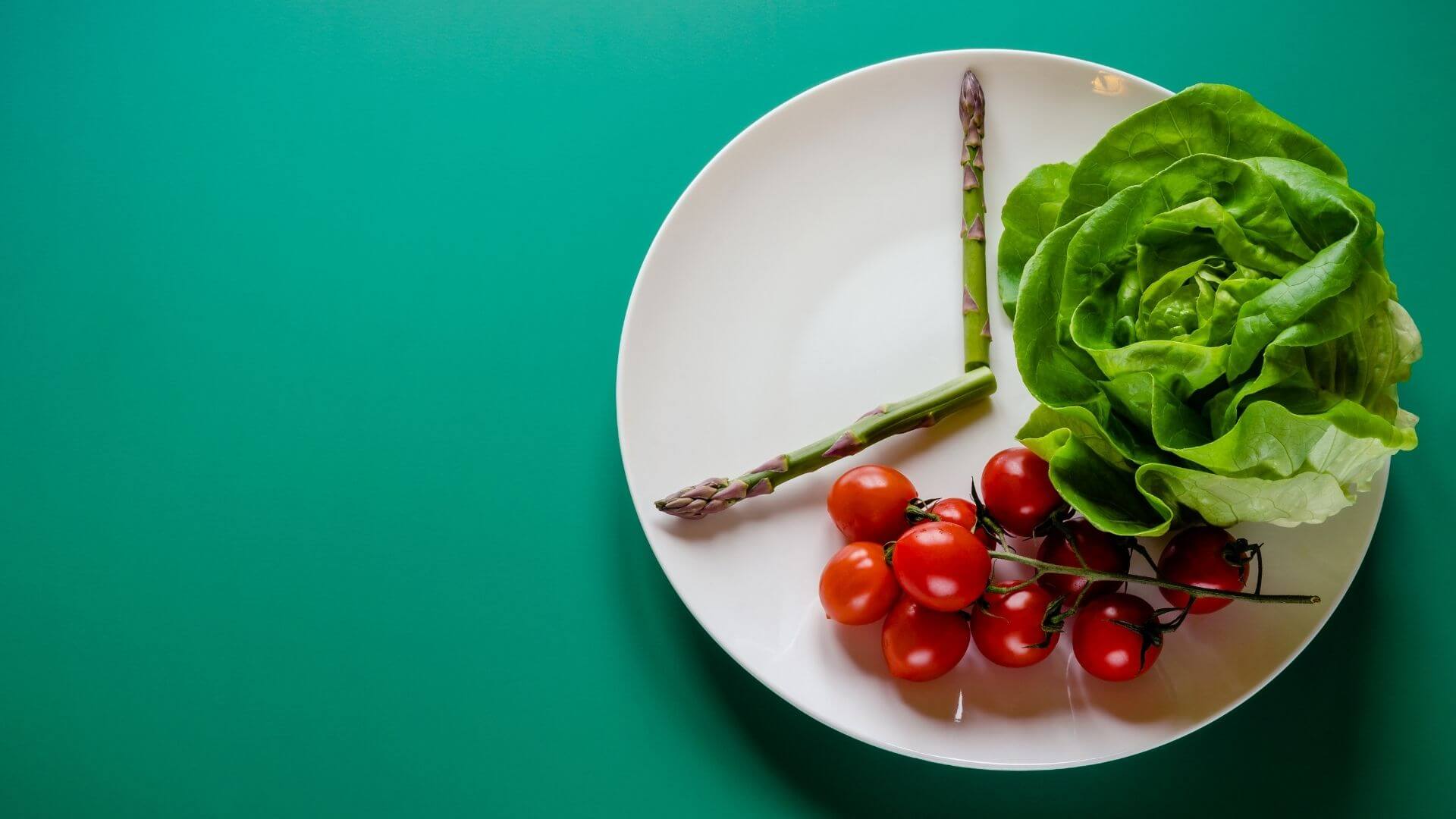 Teller mit Spargeln, Tomaten und Salat hat Aussehen einer Uhr
