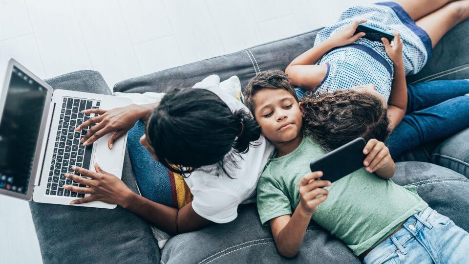 Kinder nutzen verschiedene digitale Geräte auf dem Sofa