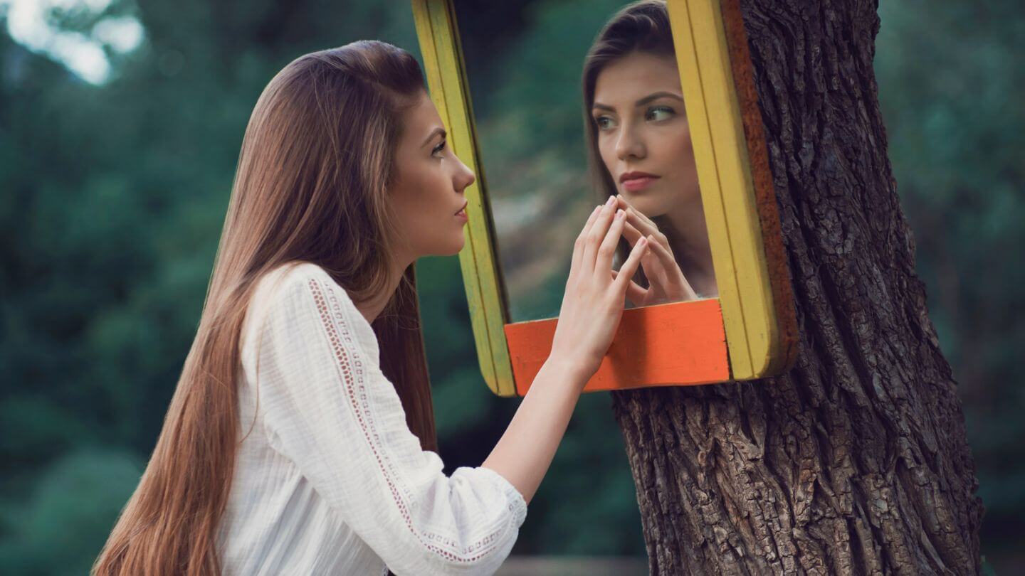 Frau schaut sich im Spiegel an - Beziehung zu dir selbst
