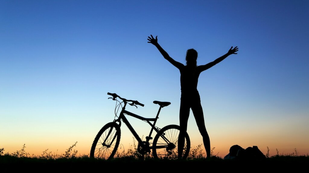 Frau mit Bike streckt sich in der Abendsonne - Was mich gesund hält